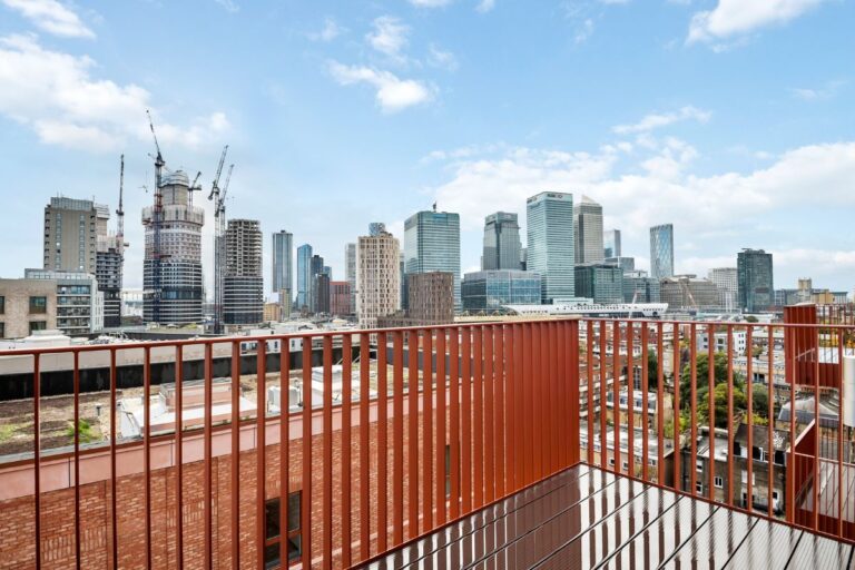 Balcony with red metal balustrade overlooking Canary Wharf skyline and surrounding buildings