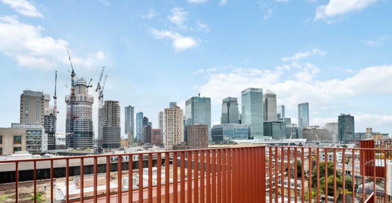 Balcony with red metal balustrade overlooking Canary Wharf skyline and surrounding buildings