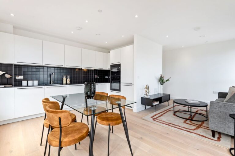 Open plan kitchen with white cabinetry, integrated oven and glass dining table