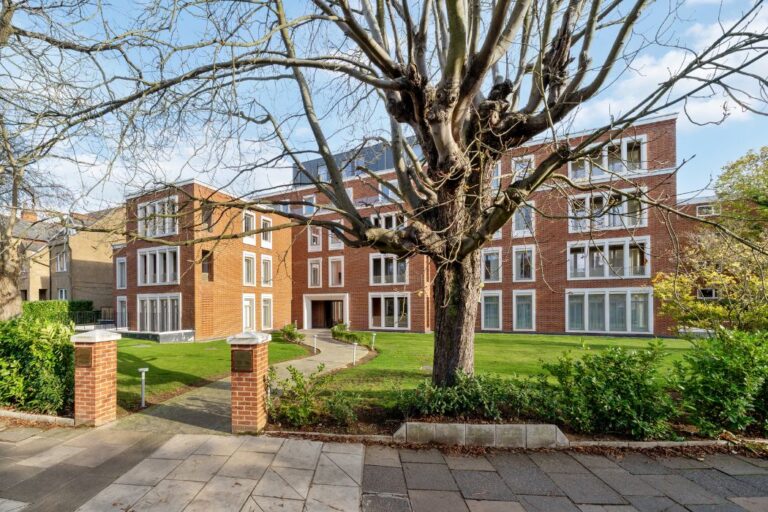 Modern red brick apartment building with landscaped entrance and mature trees
