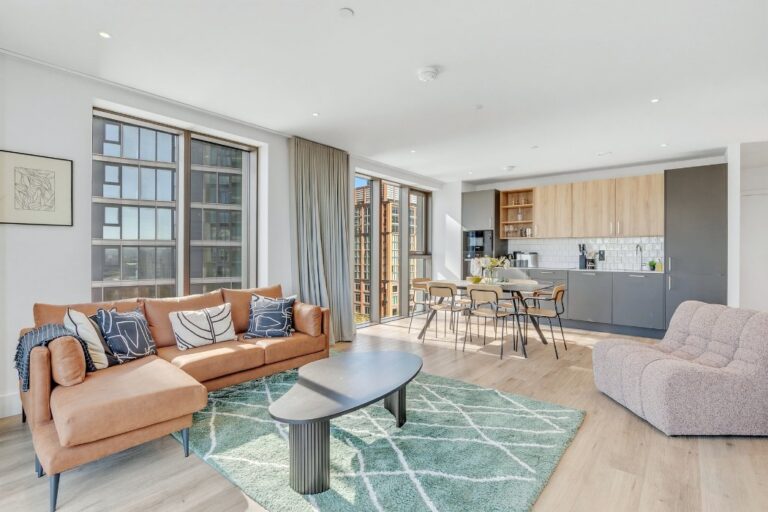 Bright open-plan living room and integrated kitchen in an apartment at 50-60 Charter Street, with wood-effect flooring and natural light from floor-to-ceiling windows
